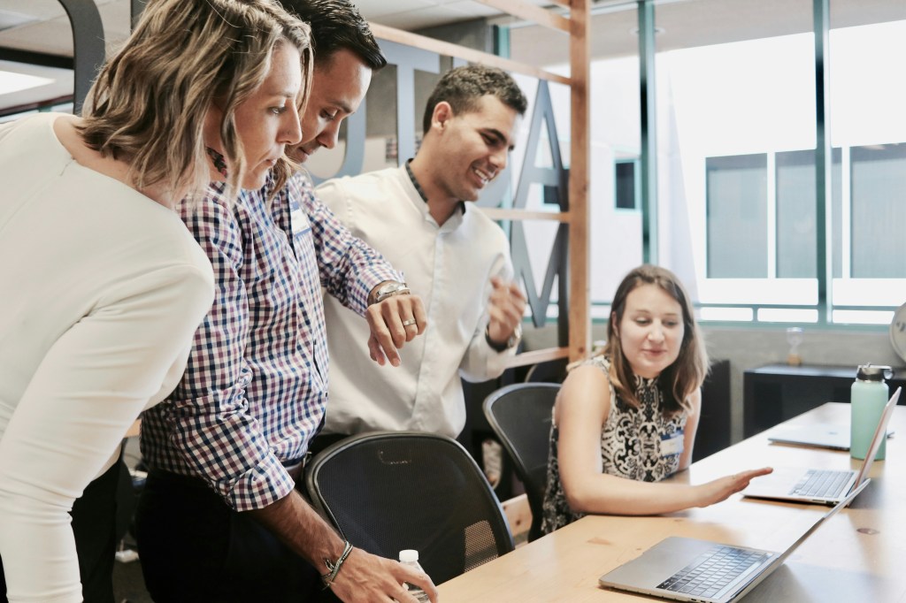 a group of people in an office looking at a computer and their watches, working together and smiling