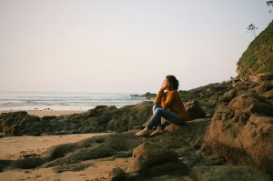 A woman sitting on a rock on the beach thinking