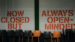 hairs in front of a wall with graffiti saying 'Now Closed' 'But Always Open Minded'